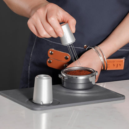 Silver Grind Logic WDT tool distributing espresso grounds in a portafilter, with matching stand beside it. 