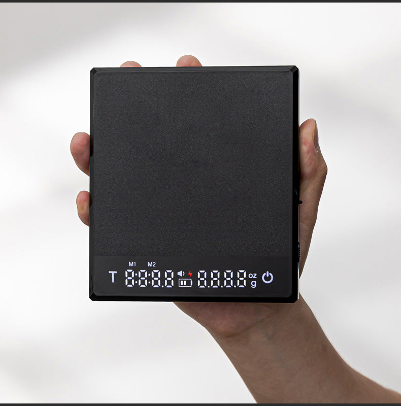 Black Grind Logic Brew Scale held in one hand, showing its compact size and digital timer display